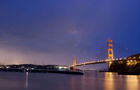 Golden Gate Bridge at night illuminated over dark water