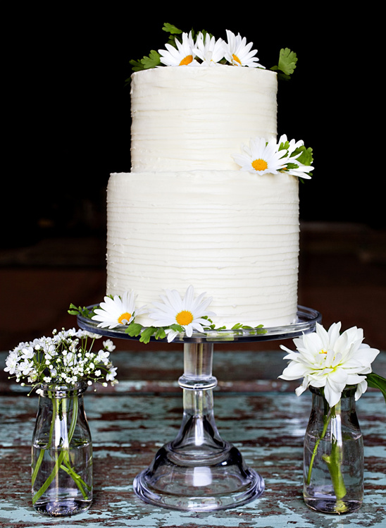Two-tiered white wedding cake with daisies