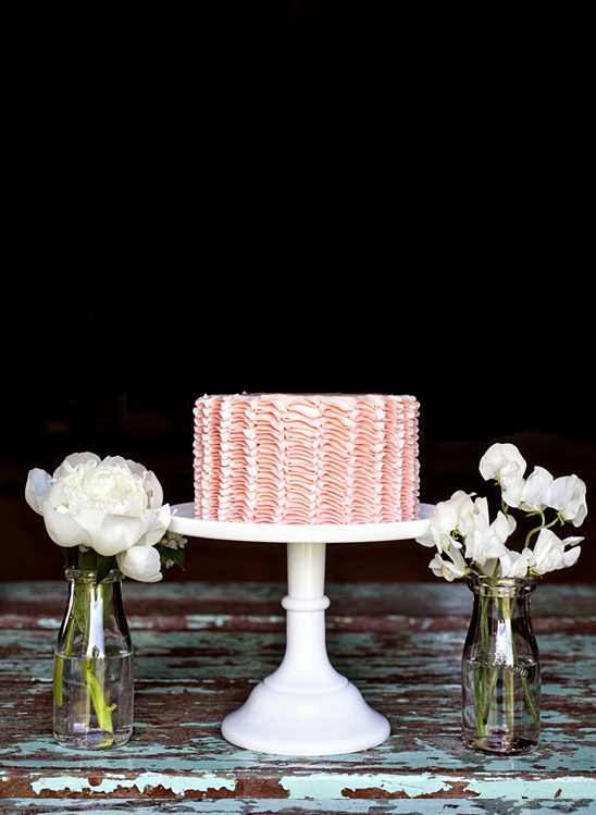 Pink ruffle cake on white stand with flowers