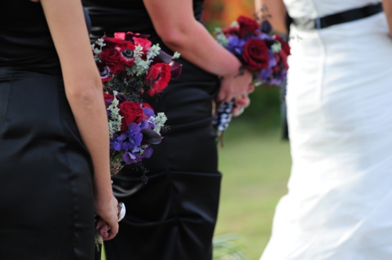 Bridesmaids hold rich red and purple bouquets