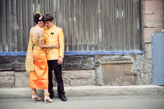 Couple in traditional yellow attire embracing near a wall