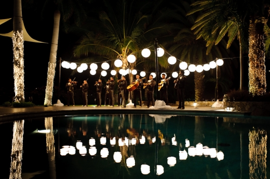 Mariachi band plays by pool at night with string lights