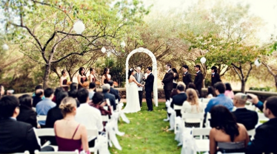 Outdoor wedding ceremony under trees, bride and groom exchanging vows