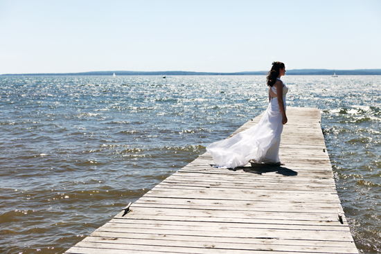 Bride in flowing gown on pier overlooking shimmering lake