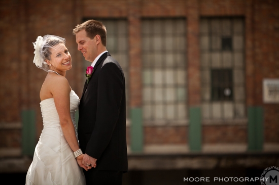 Happy bride and groom smiling near brick building