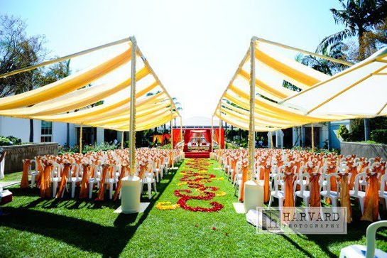 Outdoor wedding ceremony with yellow canopies and orange chairs