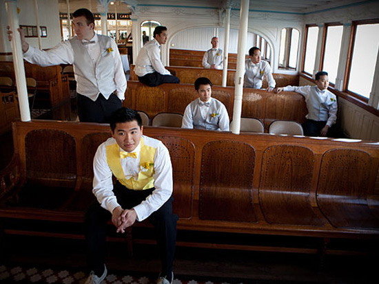 Groomsmen sit inside a boat yellow vests and bowties