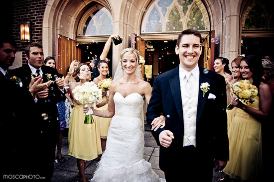 Happy couple exiting church, showered in bubbles