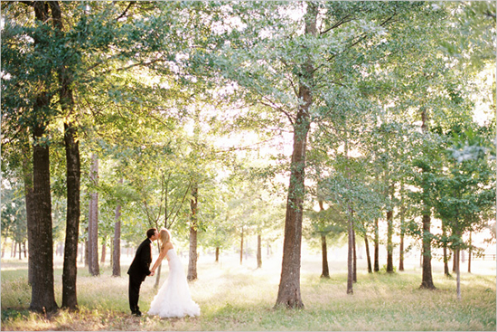 Bride and groom kissing under sunlit trees