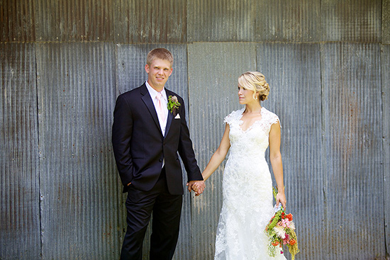 Happy newlyweds pose for wedding photo against rustic metal wall