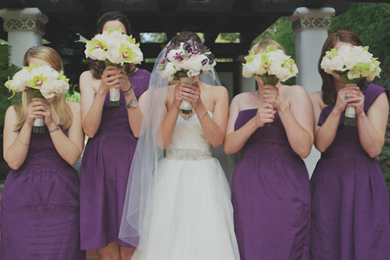 Bridesmaids in purple hide faces with wedding bouquets