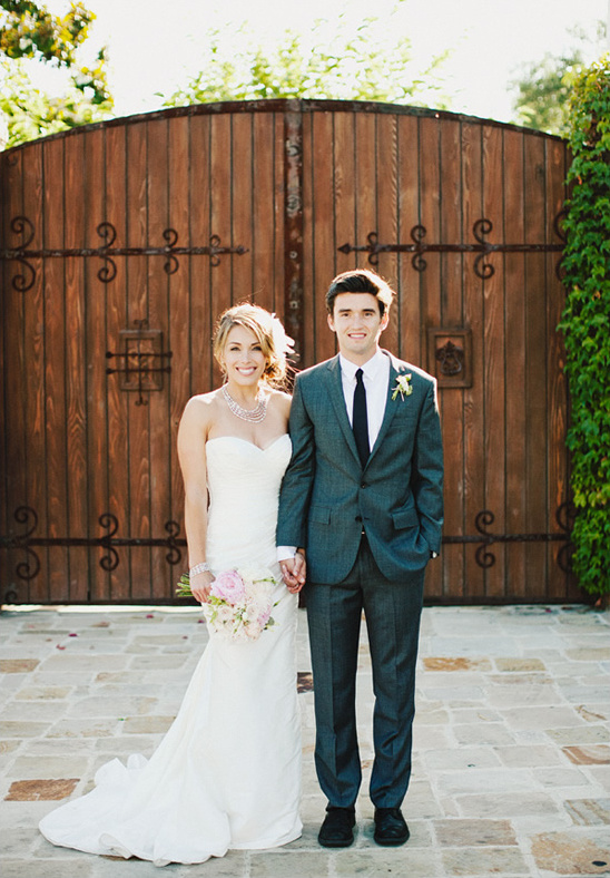 Bride and groom pose before rustic wedding gate