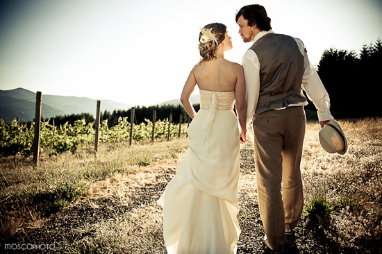 Bride and groom stroll through vineyard at sunset