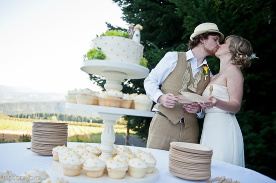 Newlyweds share a kiss by their wedding cake and cupcakes