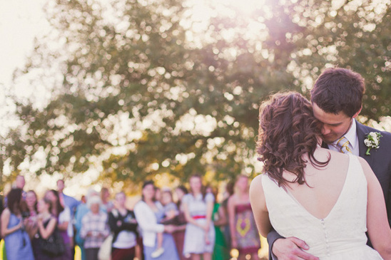 Romantic wedding couple embraces as guests look on with joy