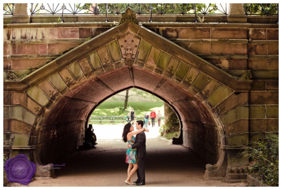 Couple embracing under a stone arch in a park setting