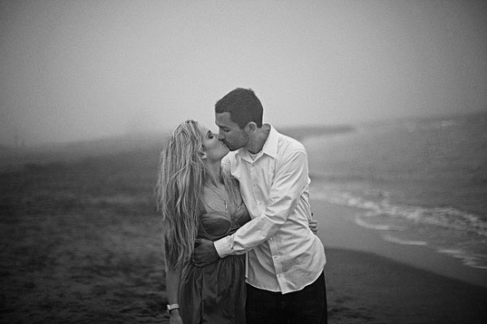 Couple sharing a romantic kiss on a misty beach in black and white