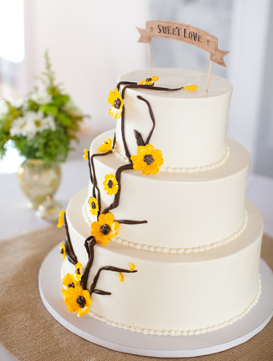 Three tiered wedding cake with yellow flower accents and sweet love banner
