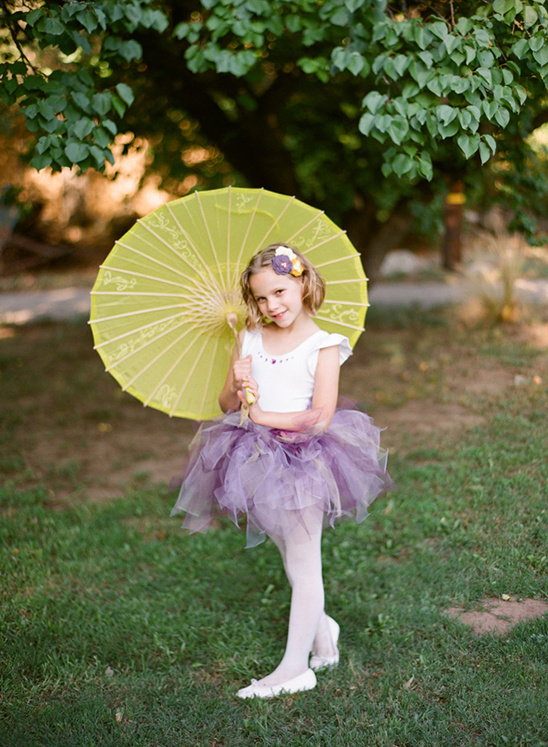 A young girl in a tutu holding a yellow parasol smiles