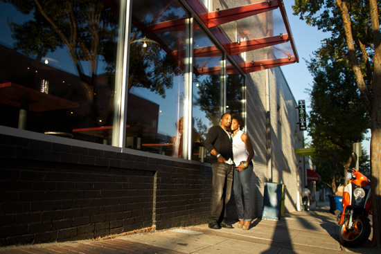 Couple stands by a building with reflected trees and scooter nearby