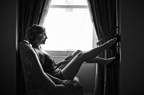 Woman in boudoir pose near window in grayscale photo