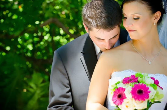 Groom kissing bride on shoulder, wedding bouquet