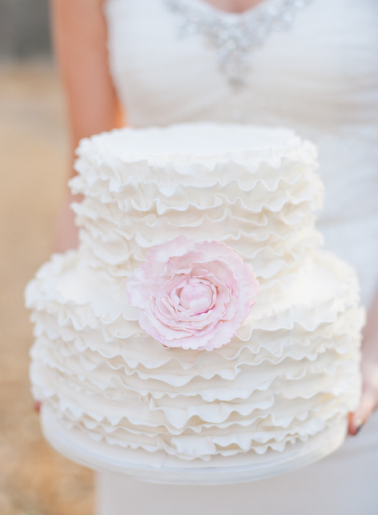 Two tier wedding cake with white ruffles and a pink flower