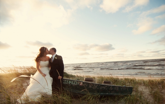 Bride and groom kiss on beach near boat at sunset
