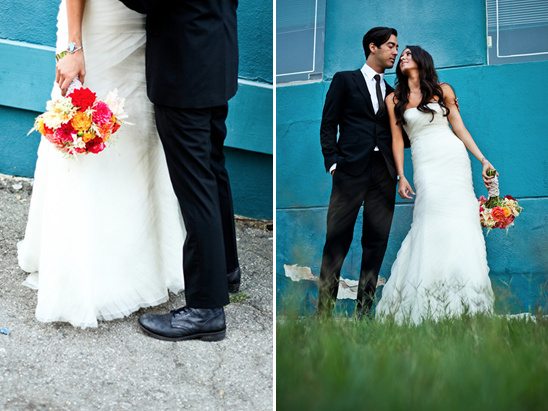 Bride and groom pose near a teal wall, holding bouquets