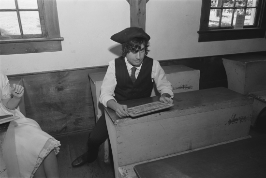 Student in colonial garb sits at school desk
