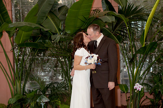 Newlyweds share a kiss surrounded by lush plants