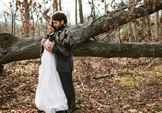 Bride and groom hug in autumn woods wearing a shawl