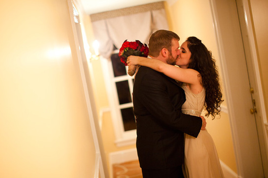 Newlyweds share a kiss with red roses hallway background