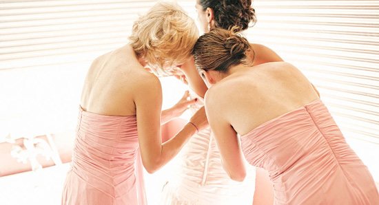 Bridesmaids helping bride dress in pink gowns