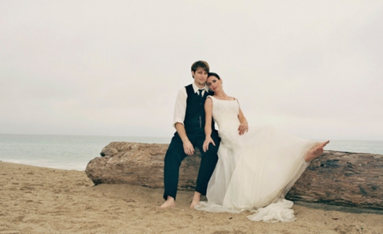 Bride and groom embracing on beach driftwood log