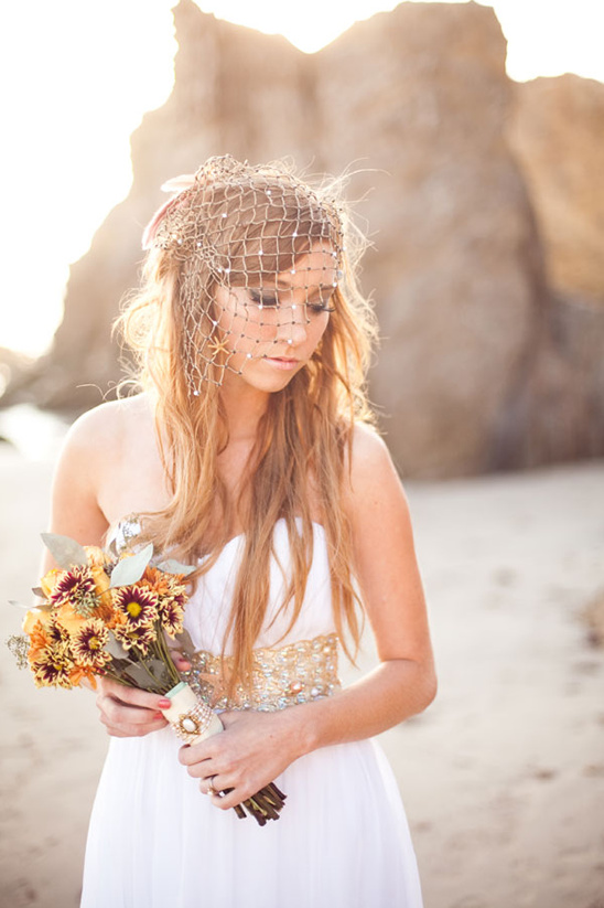 Bride in white dress holds bouquet, wearing fishnet veil