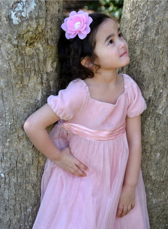 Girl in pink dress with flower looks up outdoors