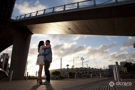 Couple embracing under a bridge at sunset with city backdrop