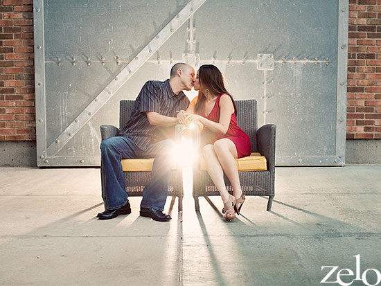 Couple kissing on a bench in front of a metal door in bright sunlight