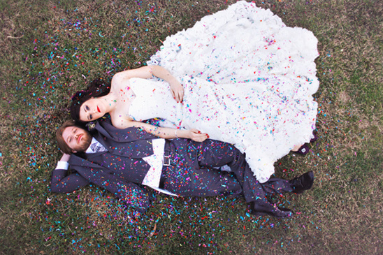 Newlyweds lying on grass covered in colorful confetti