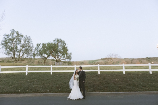 Newlyweds embrace in front of a white fence on their wedding day