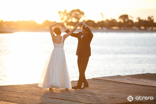 Newlyweds dancing on a dock as the sun sets over the water
