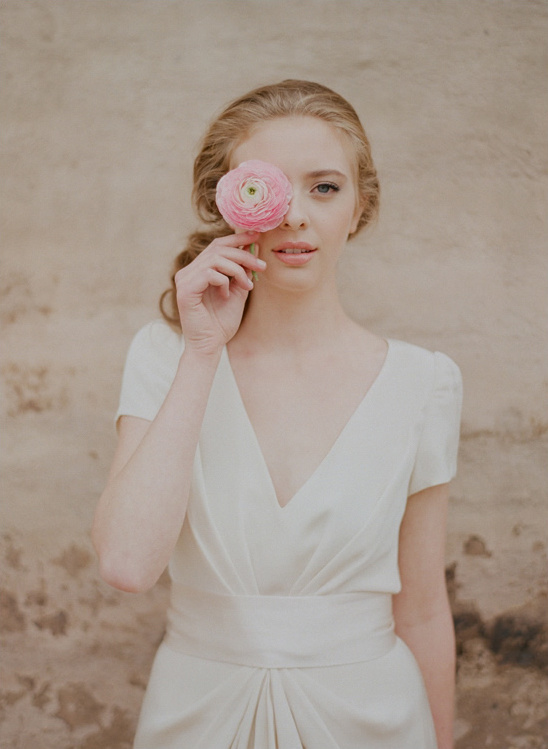 Woman in white dress holding flower over eye