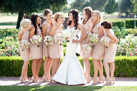Bride and bridesmaids laughing with flowers on a sunny wedding day