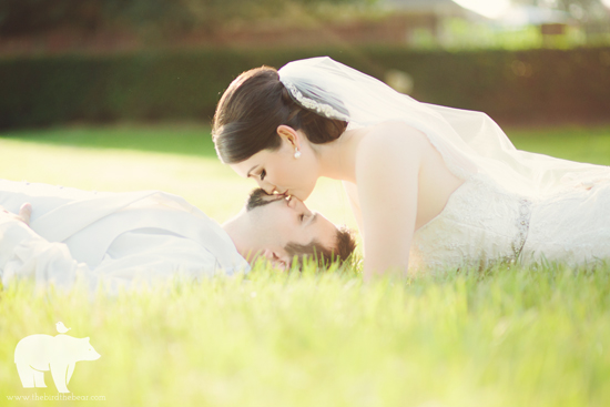 Bride lays on the ground cuddling her groom in the sunshine.