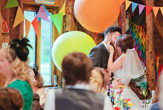 Wedding couple share a kiss, surrounded by balloons and guests