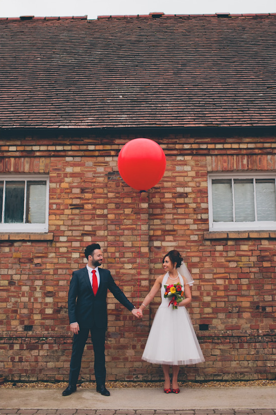 Happy couple holding hands with a red balloon at their wedding