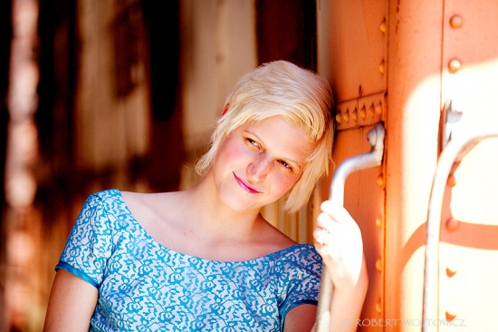 Blonde woman in blue dress leans against rustic orange wall