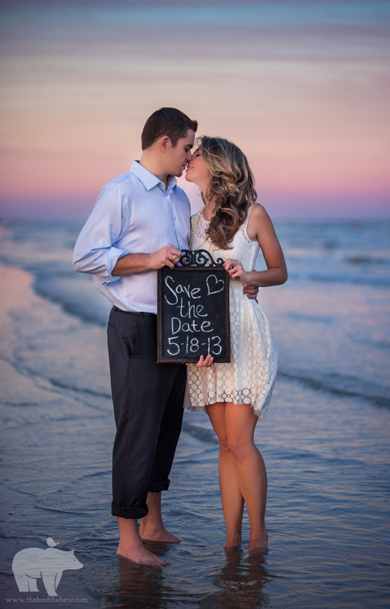 Couple kissing on beach holding a save the date sign