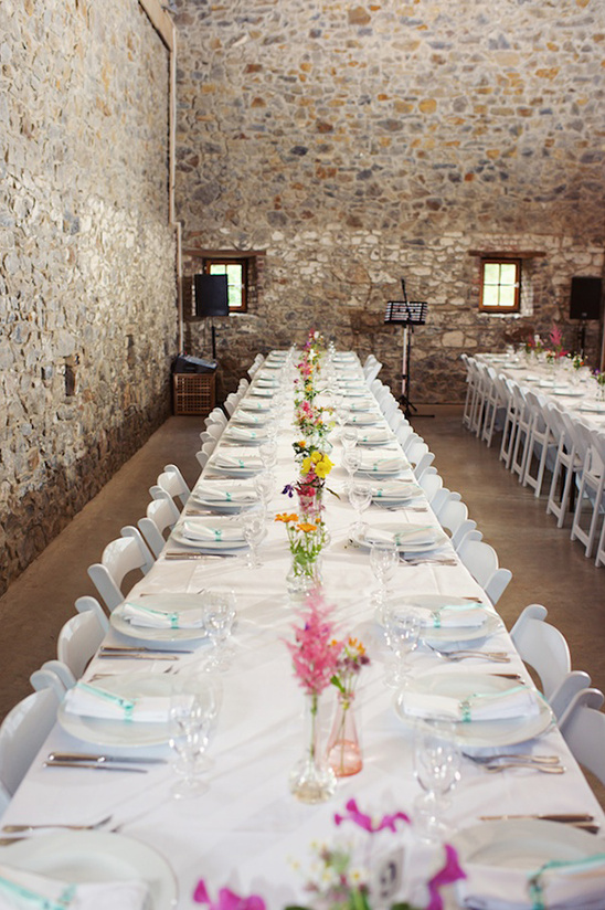 Wedding reception table set in a rustic barn with flowers